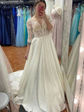 Vestido de novia largo de satén con escote en forma de A y mangas color marfil.