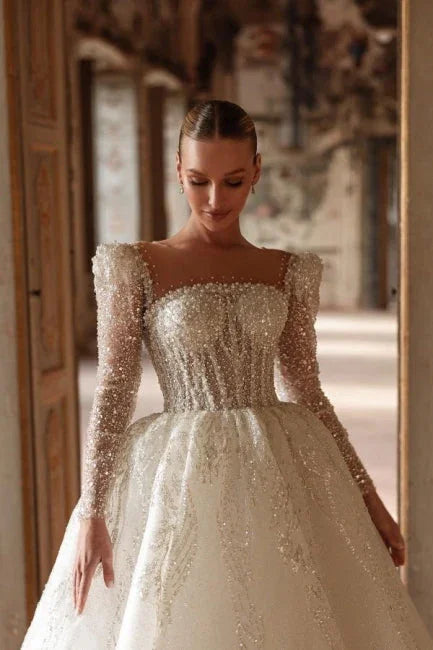 Lujoso vestido de novia largo color marfil con escote cuadrado, encaje y cuentas, y mangas largas.